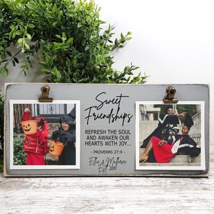 May include: A gray wooden double photo frame with two 4x4 inch openings. The frame has metal clips to hold photos and features the text "Sweet Friendships" and a quote. The frame is shown with two photos.
