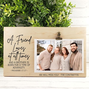 May include: A light-colored wooden photo frame with a printed quote and a photo of four people. The quote reads "A Friend Loves at all times" and "AND A BROTHER IS BORN FOR A TIME OF ADVERSITY. - PROVERBS 17:17 -"