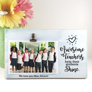 May include: A teal blue wooden picture frame with a clip to hold a photo. The frame has a white background with the text "Awesome Teachers help their students Shine."  The photo shows a group of children in school uniforms.