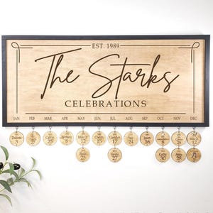 May include: A wooden family celebrations sign in a black frame. The sign reads "The Starks Celebrations" with the year "EST. 1989" above. Below are months and hanging round disks with names and dates.