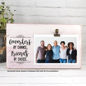 Op de afbeelding: Een wit houten fotolijstje met een clip aan de bovenkant. Het lijstje heeft een zwarte inscriptie met de tekst "Coworkers by chance, Friends by choice." Een foto van een groep vrienden is in het lijstje te zien.