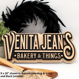 May include: A wooden sign with the text "VENITA JEANS BAKERY & THINGS." in black and natural wood. The sign is 9 inches by 18 inches.