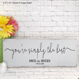 May include: A rectangular, distressed, gray wooden sign that measures 5.5" x 15". The sign reads "you're simply the best" in elegant black script. Below the text are the names "DAVID AND PATRICK" and the date "09.03.2018".