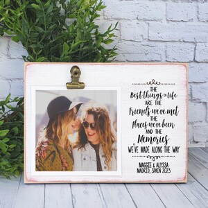 Könnte beinhalten: Ein weißer Holzfotorahmen mit einem Metallclip, der ein 10,16 x 10,16 cm großes Foto hält. Der Rahmen trägt den Text "Die besten Dinge im Leben sind die Freunde, die wir getroffen haben, die Orte, an denen wir waren, und die Erinnerungen, die wir gemacht haben". Der Rahmen ist 13,97 x 19,05 cm groß.