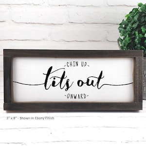 Puede incluir: Un letrero de madera enmarcado con el texto "Chin Up - Tits Out - Onward" en letras negras sobre fondo blanco. El letrero mide 7,6 cm por 20,3 cm y se muestra en un acabado de ébano.