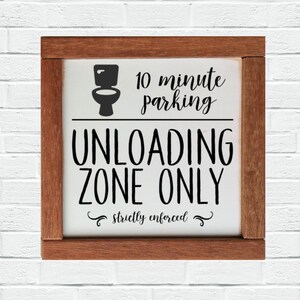 May include: A white wooden sign with a brown frame, featuring the text "10 minute parking UNLOADING ZONE ONLY strictly enforced" and a black silhouette of a toilet.