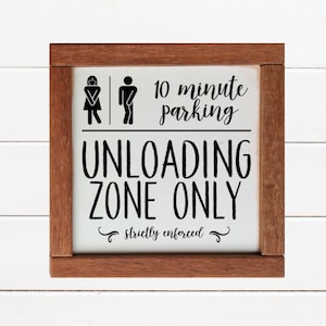 May include: A white sign with a brown wooden frame. The sign says "10 minute parking UNLOADING ZONE ONLY strictly enforced". There are also male and female restroom symbols on the sign.