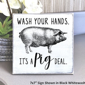 May include: A whitewashed wooden sign with black text that reads "Wash your hands. It's a Pig Deal."  A black and white illustration of a pig is in the center of the sign. The sign is 7 inches by 7 inches.