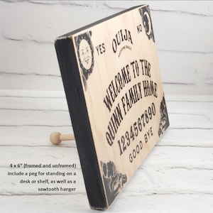 Puede incluir: Un letrero de madera con marco negro y dise&ntilde;o de tablero Ouija. El letrero dice "Bienvenido a la casa de la familia Quinn" y tiene los n&uacute;meros 1234567890 y las palabras "Adi&oacute;s" impresas en &eacute;l. El letrero mide 10,16 cm por 15,24 cm e incluye una clavija para colocarlo en un escritorio o estante, as&iacute; como un colgador de dientes de sierra.