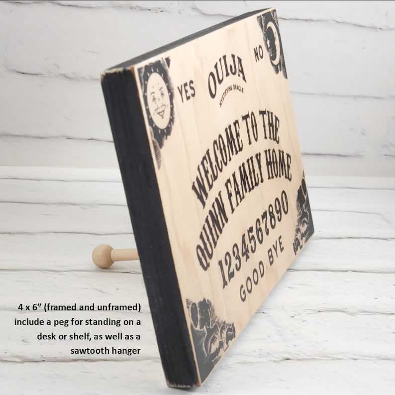 Puede incluir: Un letrero de madera con marco negro y dise&ntilde;o de tablero Ouija. El letrero dice "Bienvenido a la casa de la familia Quinn" y tiene los n&uacute;meros 1234567890 y las palabras "Adi&oacute;s" impresas en &eacute;l. El letrero mide 10,16 cm por 15,24 cm e incluye una clavija para colocarlo en un escritorio o estante, as&iacute; como un colgador de dientes de sierra.