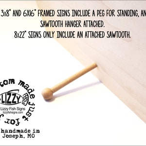 May include: A close-up of a wooden sign with a peg for standing. The sign is made of light wood and has a natural finish. The text on the sign reads "ALL 3x8" AND 6X16" FRAMED SIGNS INCLUDE A PEG FOR STANDING, AND A SAWTOOTH HANGER ATTACHED. 8x22" SIGNS ONLY INCLUDE AN ATTACHED SAWTOOTH."