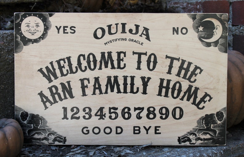 Pu&ograve; includere: Una tavola Ouija in legno con la scritta "Welcome to the Arn Family Home". La tavola presenta le parole "Yes", "No" e "Good Bye", insieme ai numeri 0-9. Grafiche decorative di sole e luna negli angoli.