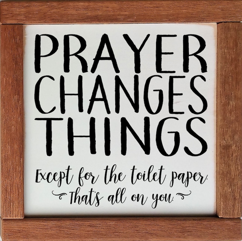 May include: A white wooden sign with black text that reads "Prayer Changes Things Except for the toilet paper. That's all on you." The sign is framed in a brown wood frame.