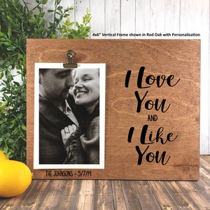 K&ouml;nnte beinhalten: Ein Holzbildrahmen mit einer schwarzen Aufschrift, die "Ich liebe dich und ich mag dich" lautet. Der Rahmen hat einen Clip zum Halten eines Fotos und einen Platz f&uuml;r die Personalisierung. Das Foto im Rahmen zeigt ein Paar.