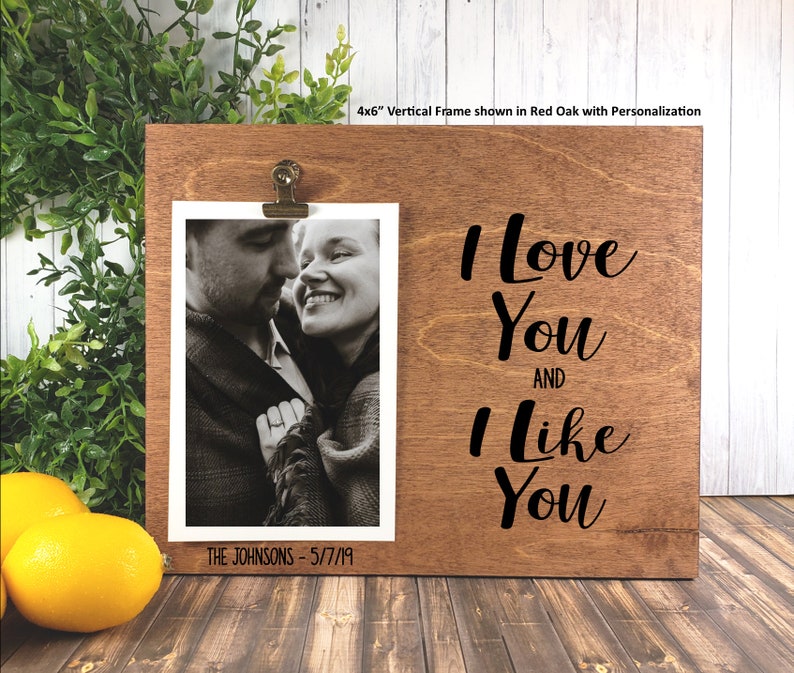 K&ouml;nnte beinhalten: Ein Holzbildrahmen mit einer schwarzen Aufschrift, die "Ich liebe dich und ich mag dich" lautet. Der Rahmen hat einen Clip zum Halten eines Fotos und einen Platz f&uuml;r die Personalisierung. Das Foto im Rahmen zeigt ein Paar.