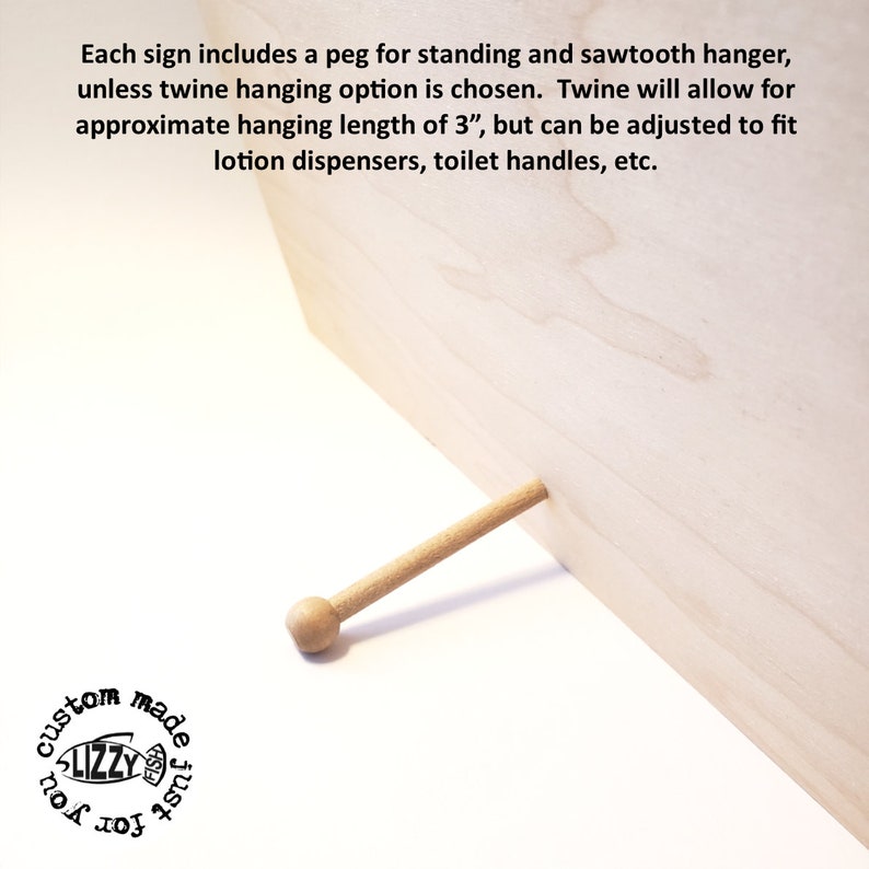 Puede incluir: Primer plano de un letrero de madera con una clavija para que se mantenga de pie. La clavija es de madera y tiene una parte superior redondeada. El letrero es de madera clara y tiene una superficie lisa. El letrero mide aproximadamente 7,6 cm de largo.