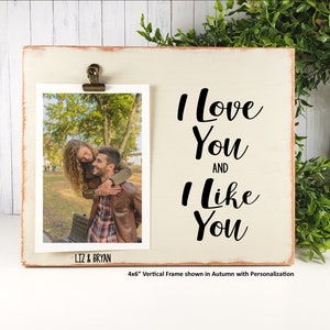 K&ouml;nnte beinhalten: Ein wei&szlig;er Holzrahmen mit einer abgenutzten Oberfl&auml;che. Der Rahmen hat oben einen Clip, um ein Foto zu halten. Das Foto zeigt ein Paar in einem Park. Der Rahmen tr&auml;gt den Text "I Love You And I Like You". Der Rahmen ist 10,2 x 15,2 cm gro&szlig;.