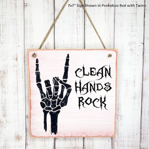 Puede incluir: Un letrero de madera de 17,8 x 17,8 cm con fondo rosa y texto negro que dice "Clean Hands Rock". Se muestra una mano de esqueleto negra haciendo el gesto de rock and roll.