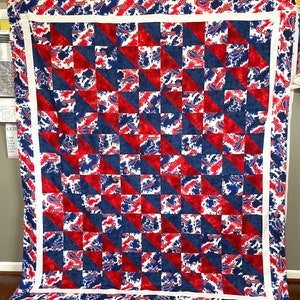 May include: A large, square quilt featuring a patchwork design in red, white, and blue. The quilt's pattern includes alternating squares of red and blue triangles, with a white border. The blue squares have a white pattern with the word "BILLS".