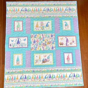 May include: A blue and purple patchwork quilt with a repeating pattern of gnomes holding Easter eggs. The quilt is made up of squares with different gnome designs, including a gnome with a basket of eggs, a gnome with a sign that says "Happy Easter", and a gnome with a butterfly.