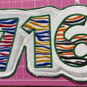 May include: Embroidered patch featuring the number "716" in a stylized design. The numbers are outlined in green with a white background. The interior of the numbers has a zebra stripe pattern in red, blue, yellow, orange, and black.