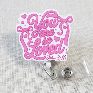 May include: Pink and white badge reel with a pink and white design that says "You are so Loved" with a heart and the text "John 3:16".