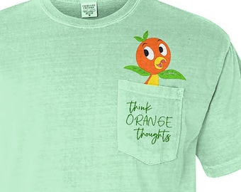 Może przedstawiać: Jasnozielony t-shirt z kieszenią, na której znajduje się kreskówkowa pomarańcza z ptasim obliczem i tekstem "Think Orange Thoughts".