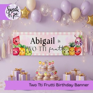 Puede incluir: Una pancarta de cumpleaños con el texto "Abigail is TWO-TTI frutti" e ilustraciones de frutas de dibujos animados. La pancarta está decorada con globos, cupcakes y cajas de regalo. La pancarta dice "Two Tti Frutti Birthday Banner".