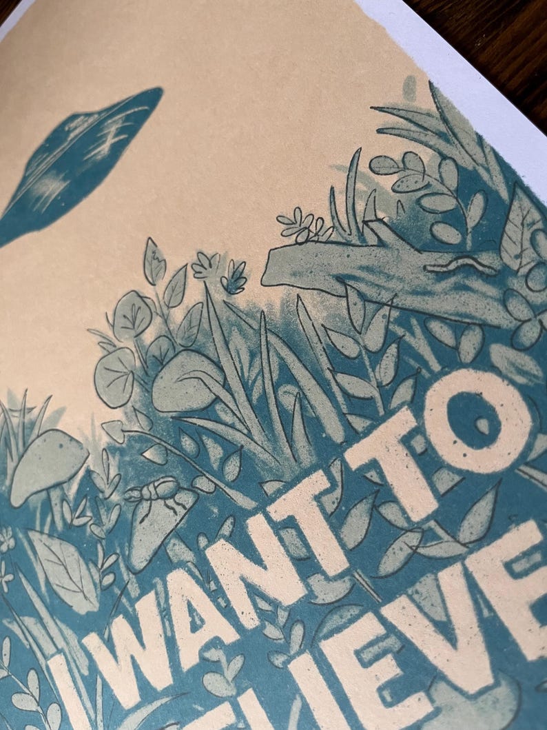May include: Illustration of a forest scene with the words "I WANT TO BELIEVE" in white block letters. The artwork features stylized plants, insects, and a leaf in shades of blue and green on a beige background.