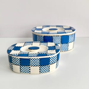 May include: Two oval ceramic containers with lids, featuring a blue and white checkered pattern. The design alternates between solid blue squares and smaller blue and white micro-checkered squares on a cream-colored base, with a blue circular knob.