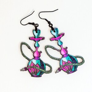 May include: A pair of colorful hookah-shaped earrings. The earrings feature a teal, pink, and purple color scheme with black ear wires. The design includes a floral pattern on the base and a green hose detail.