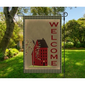 May include: A welcome garden flag featuring a red house with a black and white checked border. The house has a black bird perched on a branch and the word "WELCOME" is written vertically in red.