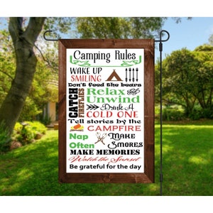 Könnte beinhalten: Ein Holzschild mit dem Text "Camping Rules" und einer Liste von Campingregeln, darunter "Wake Up Smiling", "Don't Feed the Bears", "Relax", "Unwind", "Drink a Cold One", "Tell Stories by the Campfire", "Make Smores", "Make Memories" und "Watch the Sunset".