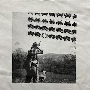 Könnte beinhalten: Ein Schwarzweißfoto einer Person, die eine Schrotflinte hält und auf etwas außerhalb des Bildes zielt. Ein Hund steht hinter der Person. Das Bild ist mit einem sich wiederholenden Muster aus pixeligen Space Invaders überlagert.