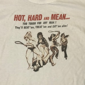 Puede incluir: Una camiseta blanca con un estampado gráfico de cuatro mujeres en estilo vintage. El texto en la camiseta dice "HOT, HARD AND MEAN... TOO TOUGH FOR ANY MAN!! They'll BEAT 'em, TREAT 'em and EAT 'em alive!"
