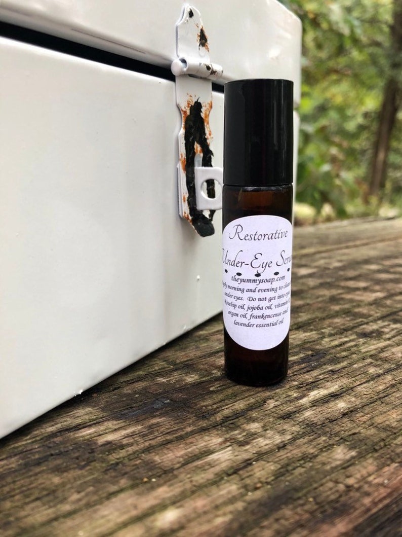 May include: A small, clear glass bottle with a black rollerball top. The bottle is labelled "Restorative Under-Eye Serum" and lists ingredients including jojoba oil, argan oil, frankincense, and lavender essential oil.