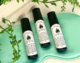 Pode incluir: Três frascos de rolo pretos com rótulos brancos que dizem "Under Eye Serum" sobre uma superfície de cetim azul claro. Os frascos são de 10 ml cada.