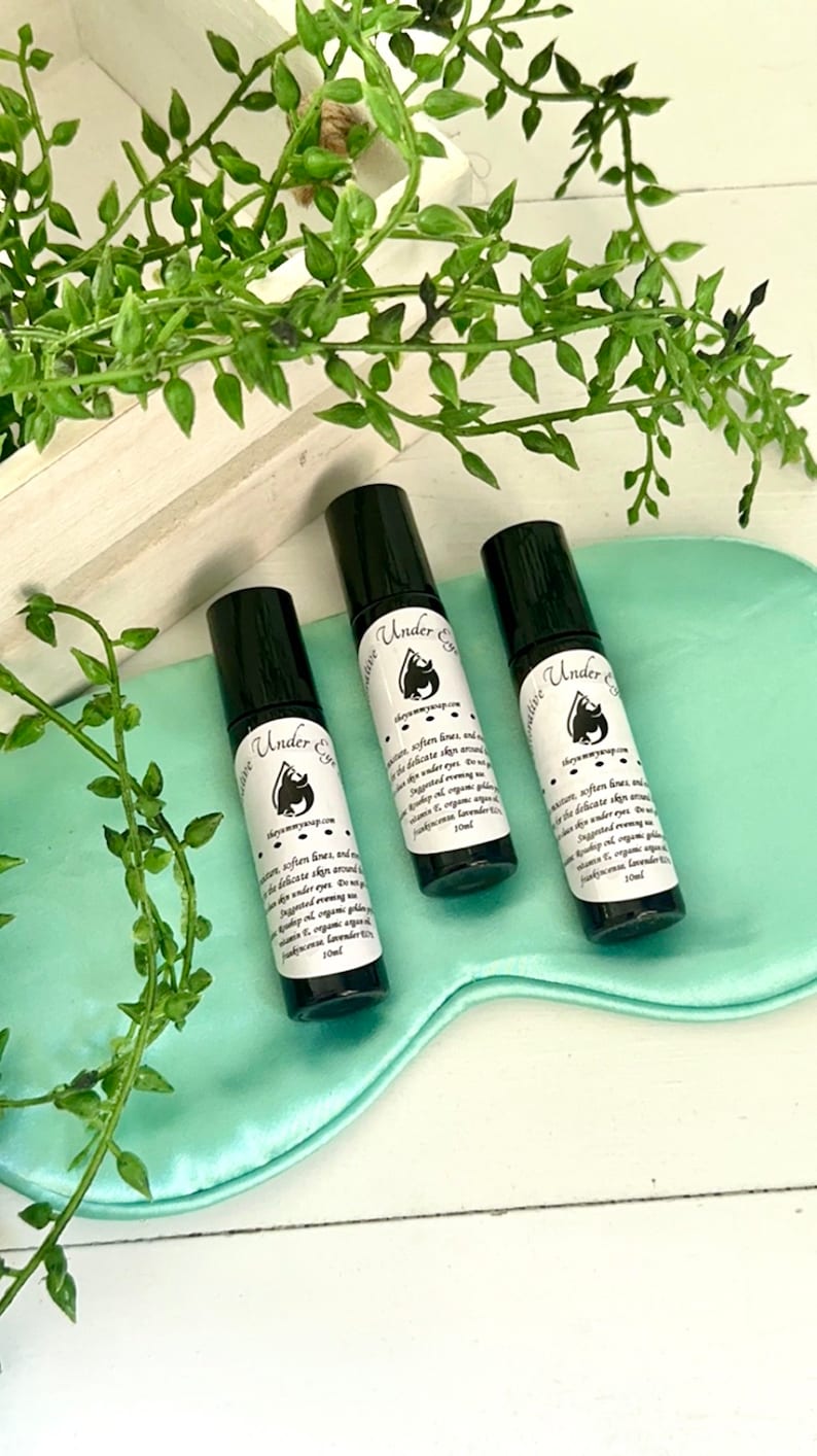 May include: Three black roller bottles with white labels that say "Under Eye Serum" on a light blue satin surface. The bottles are 10 ml each.