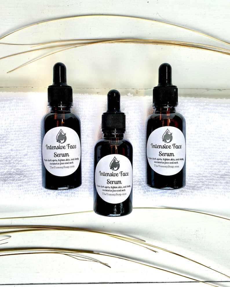 May include: Three brown glass bottles of Intensive Face Serum with black droppers. Each bottle has a white label with a logo and text. The text reads: "Fade dark spots, tighten skin, and deeply moisturize face and neck. TheYummySoap.com."