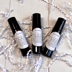 May include: Three small black glass bottles with white labels that say "Restorative Under-Eye Serum" and list ingredients. The bottles are sitting on a white surface with white paper shreds.