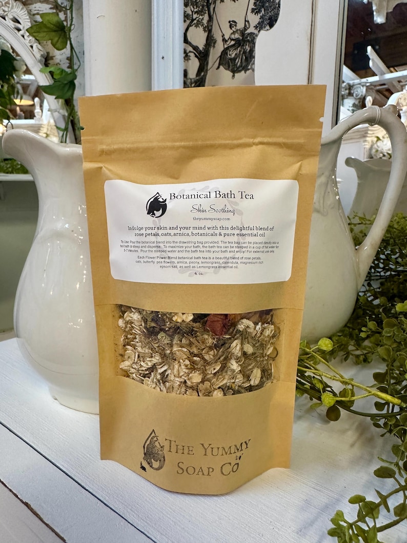 May include: A brown paper pouch of Botanical Bath Tea with a clear window showing dried rose petals, oats, and botanicals. The label features the text Botanical Bath Tea, Skin Soothing, and The Yummy Soap Co, along with usage instructions and ingredients.