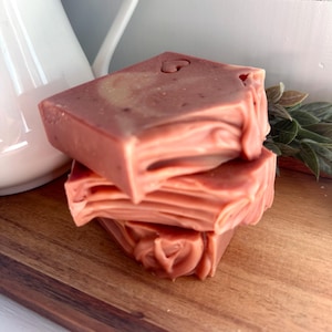 May include: A stack of three rectangular bars of soap in a muted dusty rose color. The soap features a smooth top surface with a small heart-shaped indentation and layered, wavy textures along the sides of each individual bar.