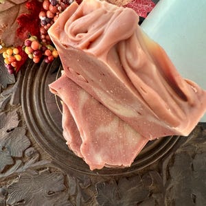 May include: Two stacked bars of handmade soap with a marbled, dusty rose and cream-colored surface. The top bar features a swirled, textured peak, while the bottom bar shows a smooth, layered cross-section with subtle white speckles.