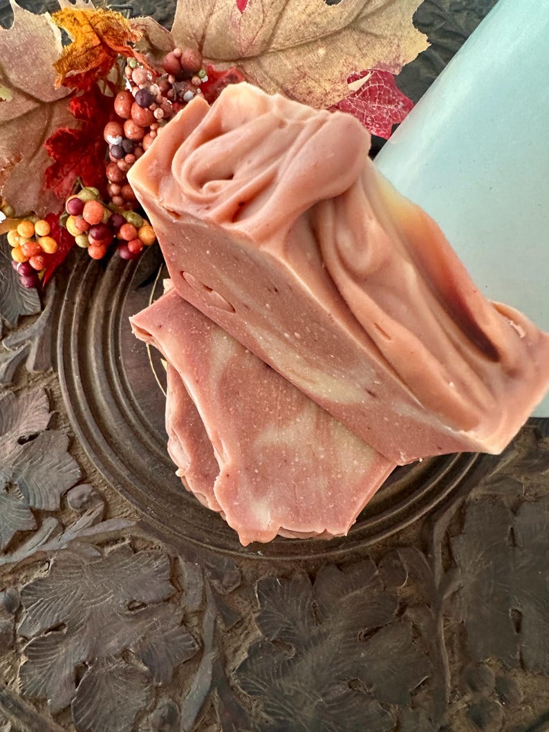 May include: Two stacked bars of handmade soap with a marbled, dusty rose and cream-colored surface. The top bar features a swirled, textured peak, while the bottom bar shows a smooth, layered cross-section with subtle white speckles.