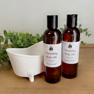 May include: Two amber glass bottles with black caps and white labels. The labels read "Nourishing Body Oils" with the scent names "Sweet Romance" and "Lovely Lavender". Each bottle contains 4 oz of oil.