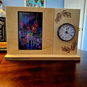 May include: A wooden picture frame with a colorful image of a castle and a clock on the right side. The frame is on a wooden base.