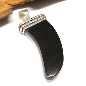 May include: A black pendant with a curved, claw-like shape. The pendant has a silver bail and a silver border with small, round details. The pendant is set against a white background.