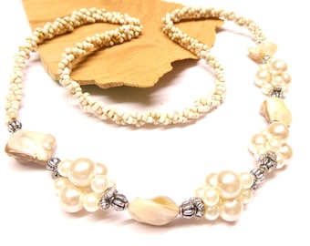 May include: A white pearl and shell necklace with silver accents. The necklace is made with small white beads and features clusters of pearls and shell pieces.
