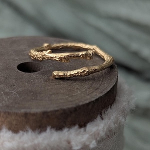 May include: A gold twig ring on a wooden spool wrapped in white fabric.