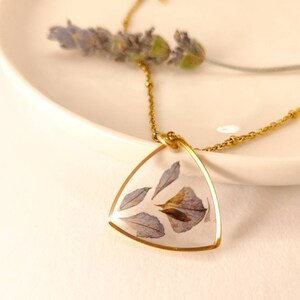 May include: A gold chain necklace with a triangular pendant featuring pressed purple flowers encased in clear resin.